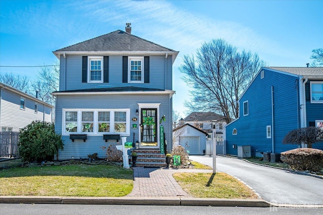 view of front of home with an outbuilding, aphalt driveway, a front yard, a garage, and a chimney