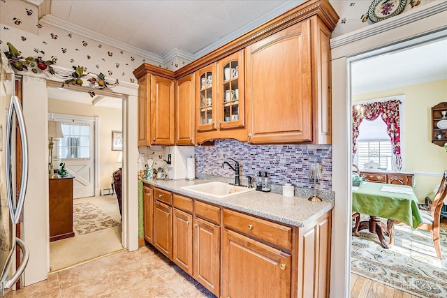 kitchen featuring tasteful backsplash, glass insert cabinets, ornamental molding, brown cabinets, and a sink