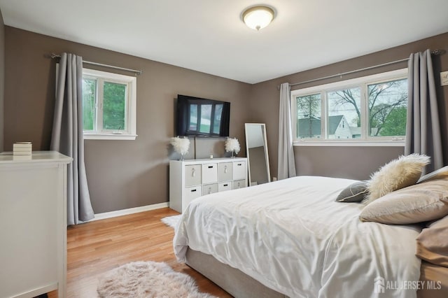 bedroom with baseboards, multiple windows, and light wood finished floors
