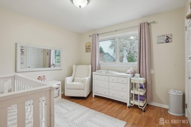 bedroom with baseboards, a nursery area, and wood finished floors