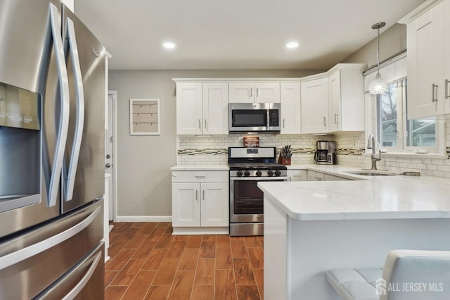 kitchen with white cabinets, appliances with stainless steel finishes, light stone counters, a sink, and backsplash