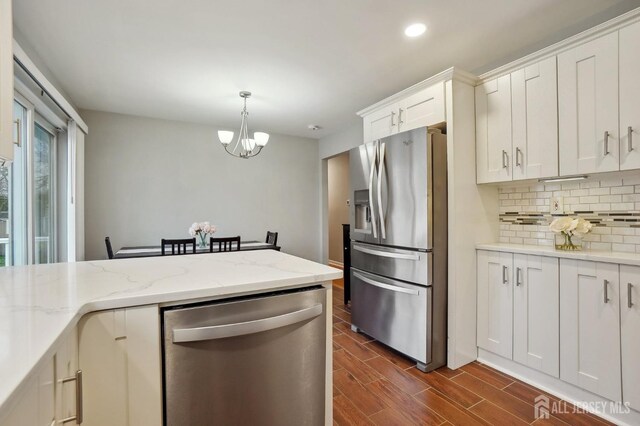 kitchen with tasteful backsplash, dark wood-style flooring, appliances with stainless steel finishes, a chandelier, and white cabinetry