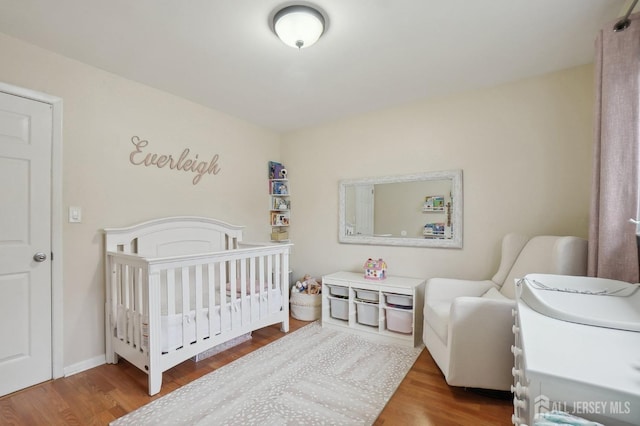 bedroom with a crib, baseboards, and wood finished floors