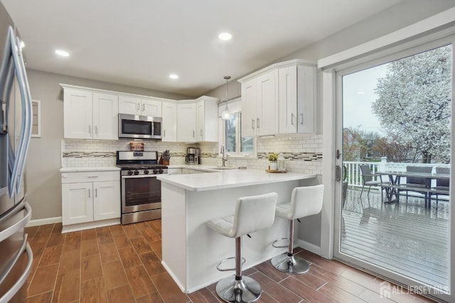 kitchen featuring a peninsula, appliances with stainless steel finishes, decorative backsplash, and a sink