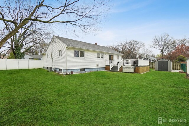 rear view of property featuring a wooden deck, a fenced backyard, an outdoor structure, a lawn, and a storage unit