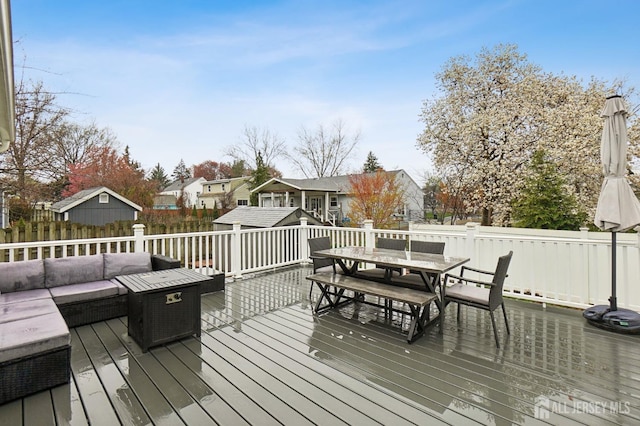 wooden deck featuring an outbuilding, a shed, fence, outdoor dining space, and a residential view