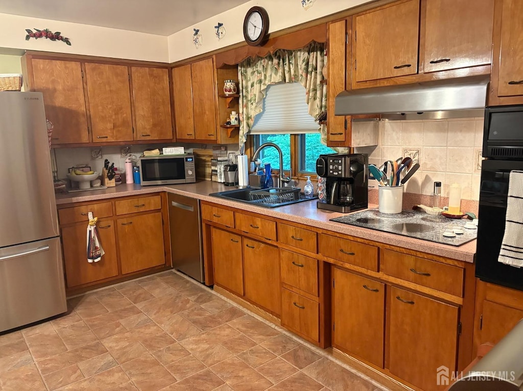 kitchen featuring stainless steel appliances, a sink, under cabinet range hood, brown cabinets, and light countertops