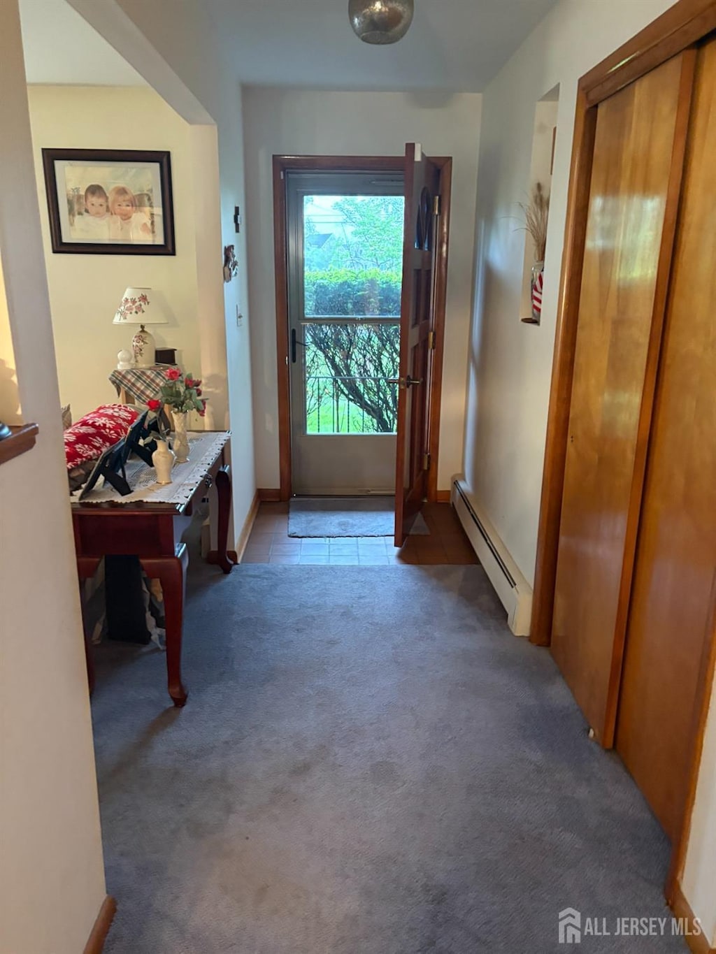 doorway featuring a baseboard heating unit, carpet floors, and baseboards