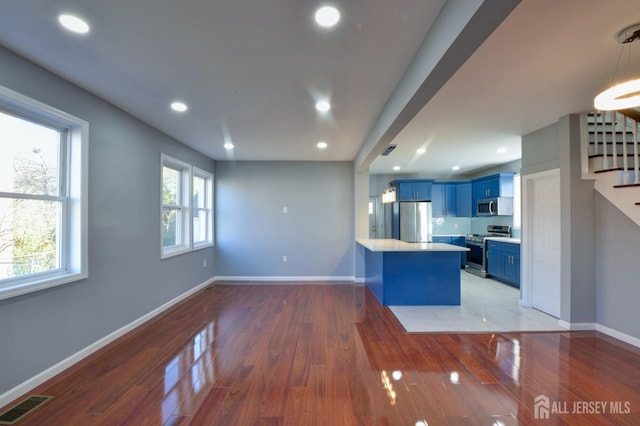 kitchen featuring blue cabinetry, decorative light fixtures, dark hardwood / wood-style flooring, kitchen peninsula, and stainless steel appliances