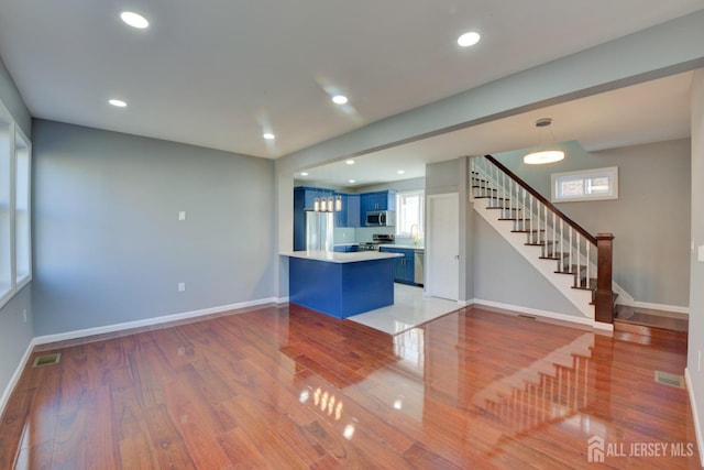 kitchen featuring kitchen peninsula, stainless steel appliances, blue cabinets, hardwood / wood-style flooring, and a breakfast bar area