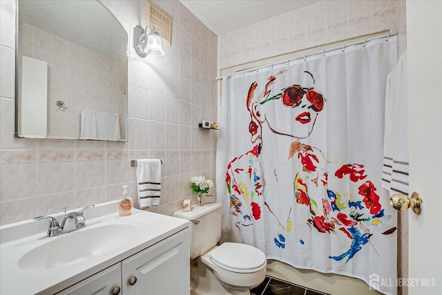 bathroom with toilet, vanity, a textured ceiling, and tile walls
