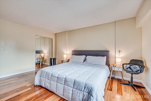 bedroom with a textured ceiling, wood finished floors, a closet, and baseboards