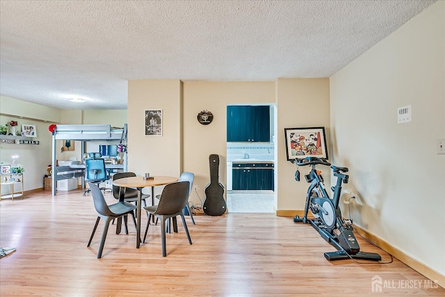 dining area with light wood-style flooring, baseboards, and a textured ceiling