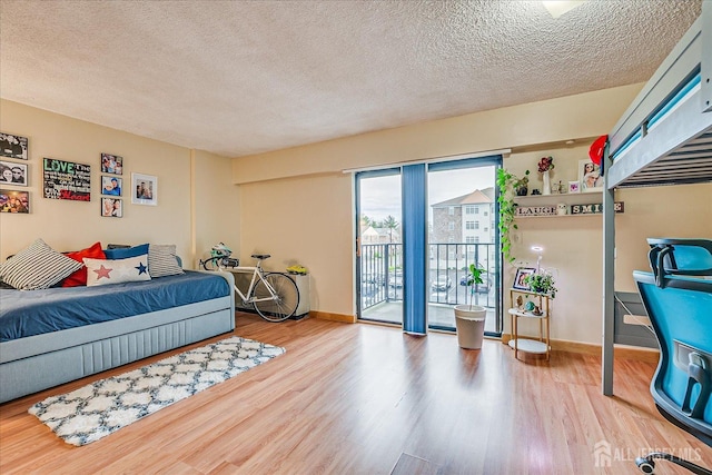bedroom featuring baseboards, wood finished floors, access to outside, and a textured ceiling
