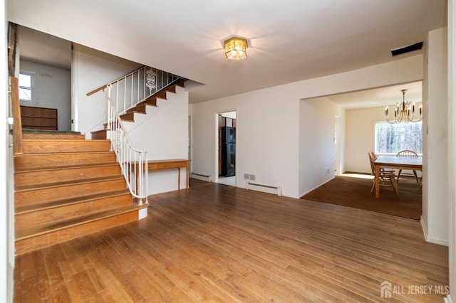 unfurnished living room featuring a baseboard radiator, wood finished floors, and a notable chandelier