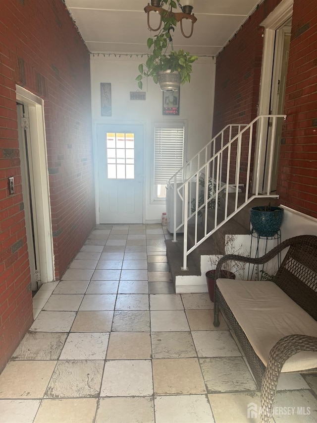 foyer entrance with stairs, brick wall, and stone tile flooring