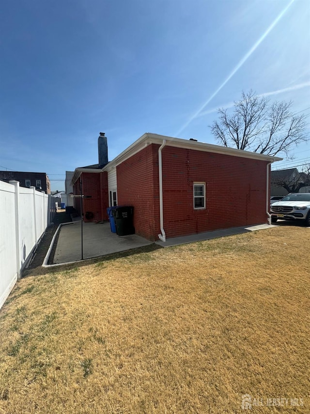 exterior space with brick siding, fence, a chimney, a yard, and a patio area