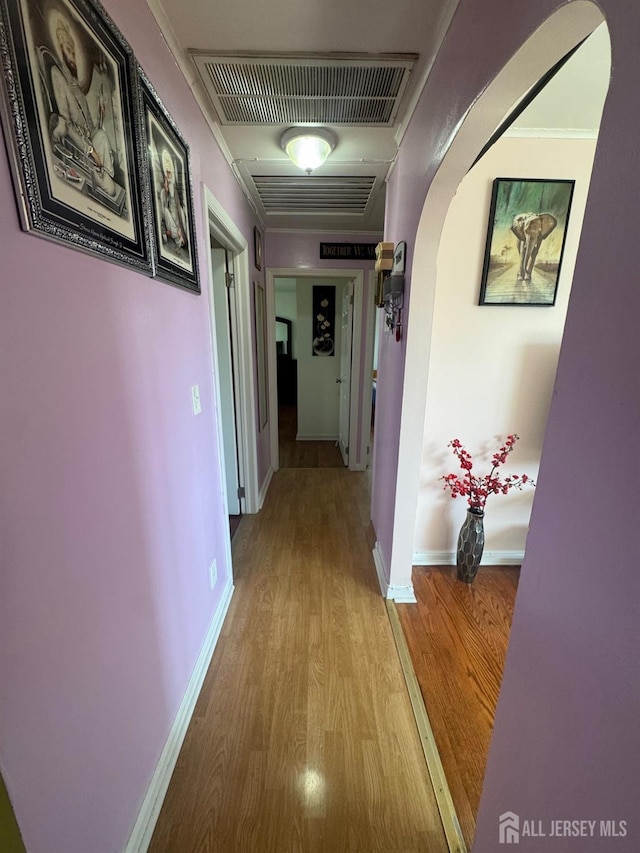 corridor with visible vents, arched walkways, light wood finished floors, and baseboards