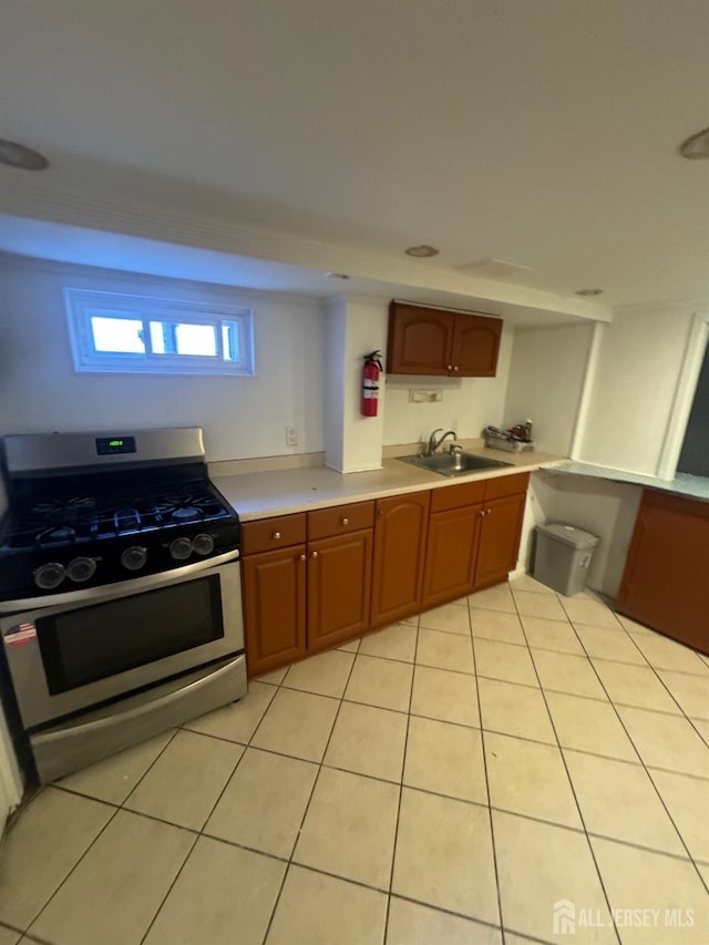 kitchen with a sink, gas stove, brown cabinetry, light countertops, and light tile patterned floors