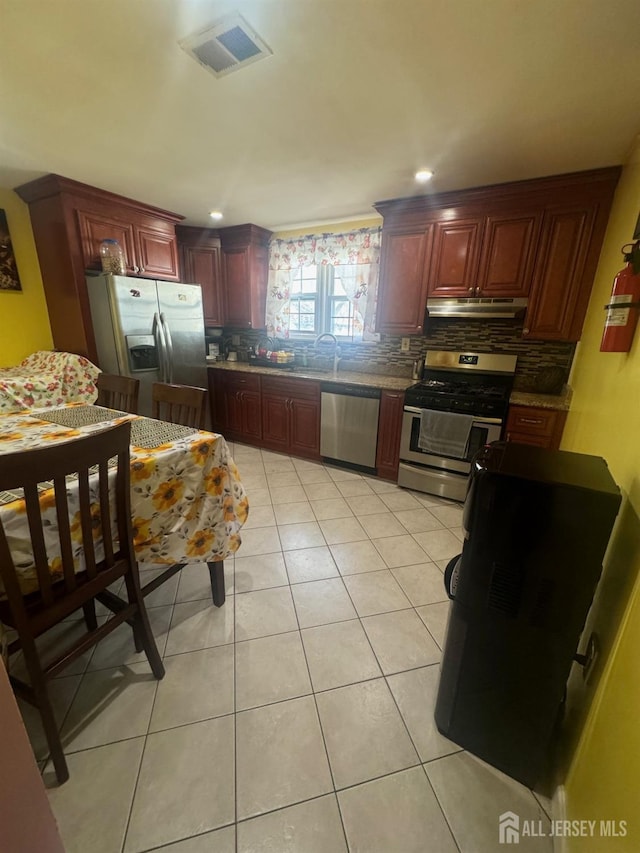 kitchen featuring visible vents, light tile patterned flooring, stainless steel appliances, under cabinet range hood, and reddish brown cabinets