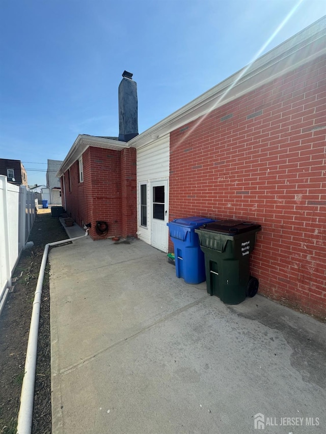 view of side of home with fence, brick siding, and a chimney