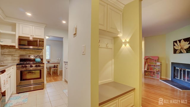 2413 Old Stone Mill Dr, East Windsor, NJ 08512 - kitchen with appliances with stainless steel finishes, open shelves, backsplash, a lit fireplace, and light countertops