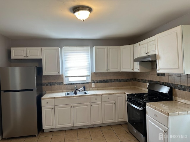 kitchen featuring tile counters, black gas range, freestanding refrigerator, a sink, and under cabinet range hood