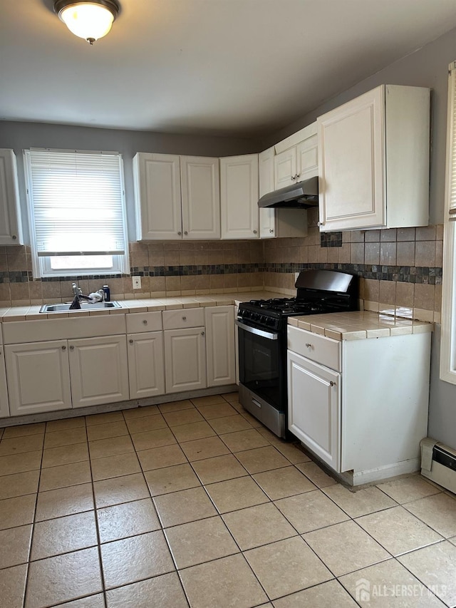 kitchen with white cabinets, range with gas stovetop, tile countertops, a sink, and light tile patterned flooring