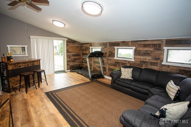 living room featuring wooden walls, light hardwood / wood-style flooring, ceiling fan, and vaulted ceiling