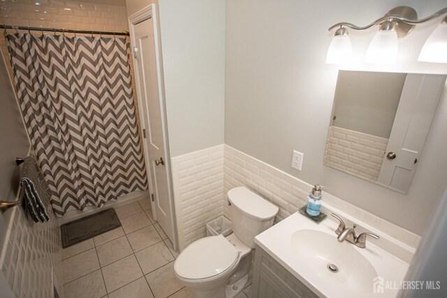 bathroom with a shower with curtain, tile patterned flooring, toilet, vanity, and tile walls