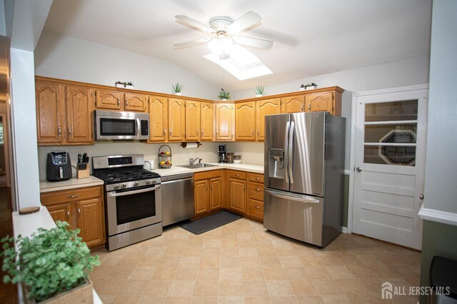 kitchen with vaulted ceiling with skylight, ceiling fan, sink, and appliances with stainless steel finishes