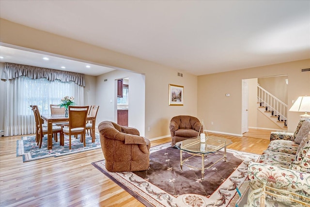 living room with light wood-style floors, stairway, visible vents, and baseboards