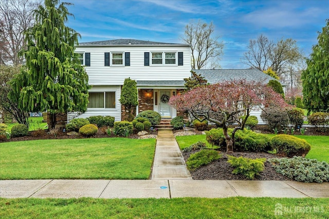 view of front facade featuring a front lawn, roof with shingles, and brick siding