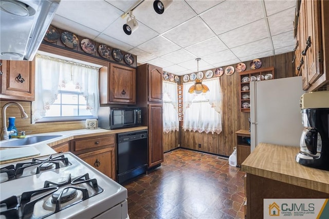 kitchen with black appliances, a paneled ceiling, sink, and wooden walls