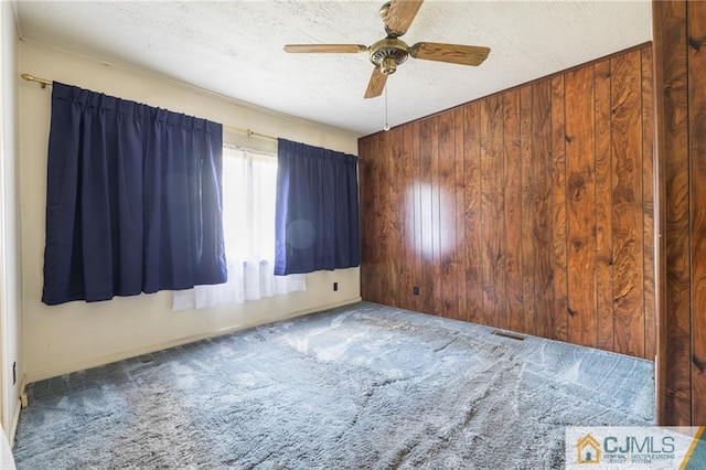 spare room featuring carpet flooring, ceiling fan, wood walls, and a textured ceiling