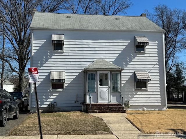 view of front facade with a shingled roof, entry steps, and a chimney