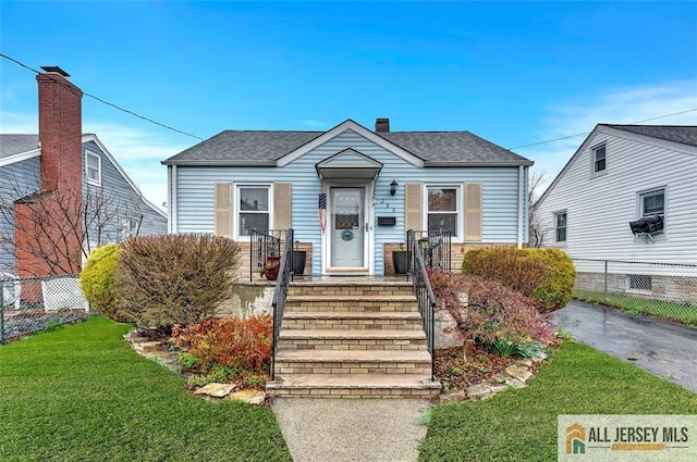 view of front of home with a chimney, fence, roof with shingles, and a front yard