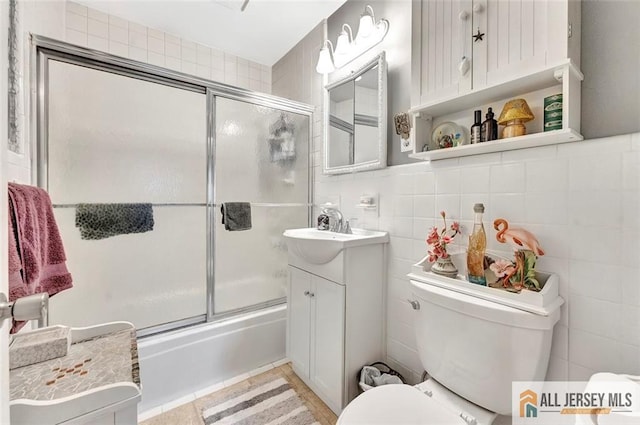 full bath with tile walls, vanity, enclosed tub / shower combo, and toilet