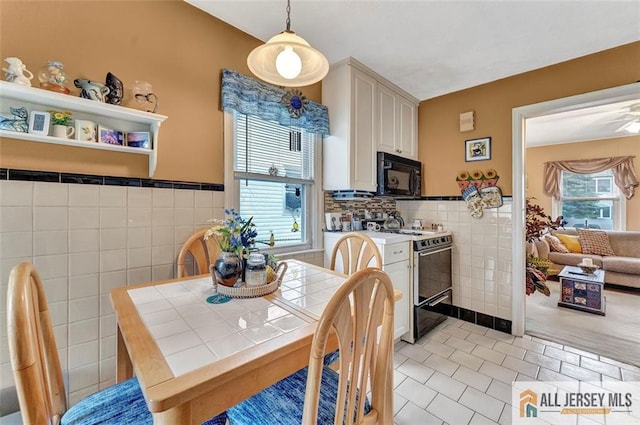 kitchen featuring tile counters, gas range oven, light tile patterned flooring, black microwave, and tile walls