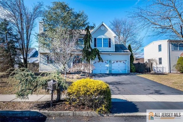 traditional-style house featuring aphalt driveway, a chimney, an attached garage, and fence