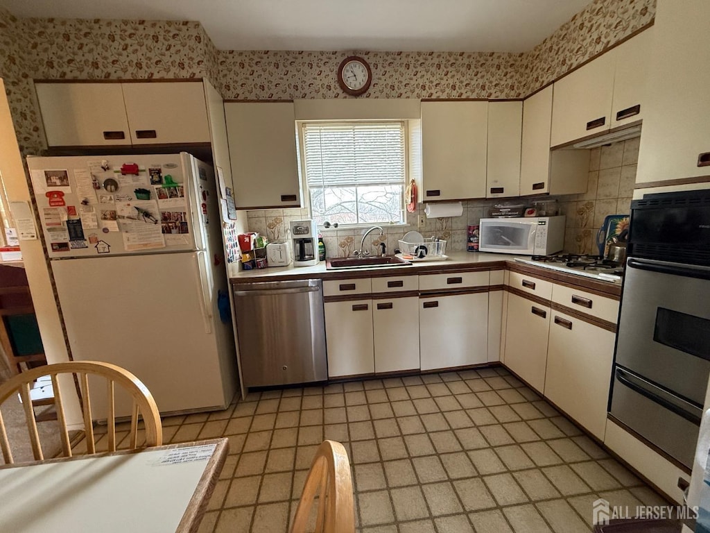 kitchen with tasteful backsplash, white appliances, white cabinetry, and a sink