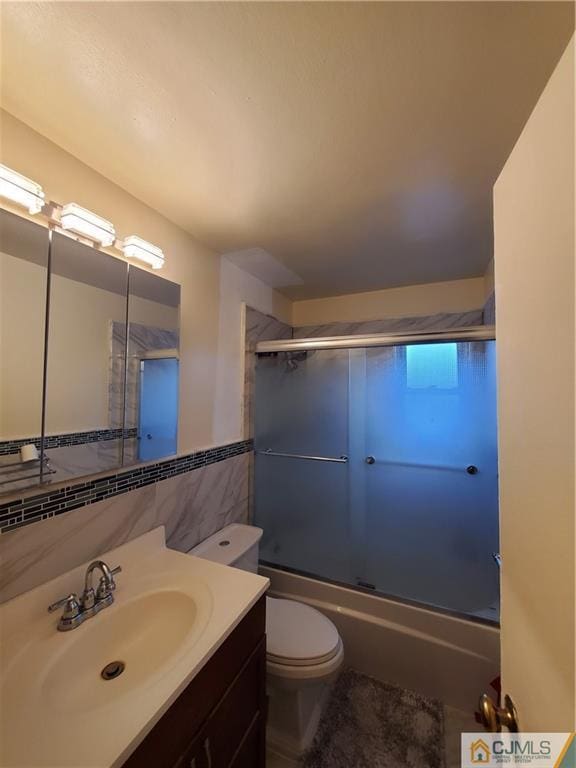 full bathroom with toilet, enclosed tub / shower combo, tile walls, and vanity