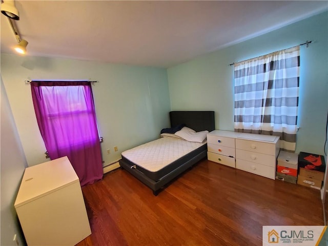 bedroom with track lighting, baseboard heating, and wood finished floors