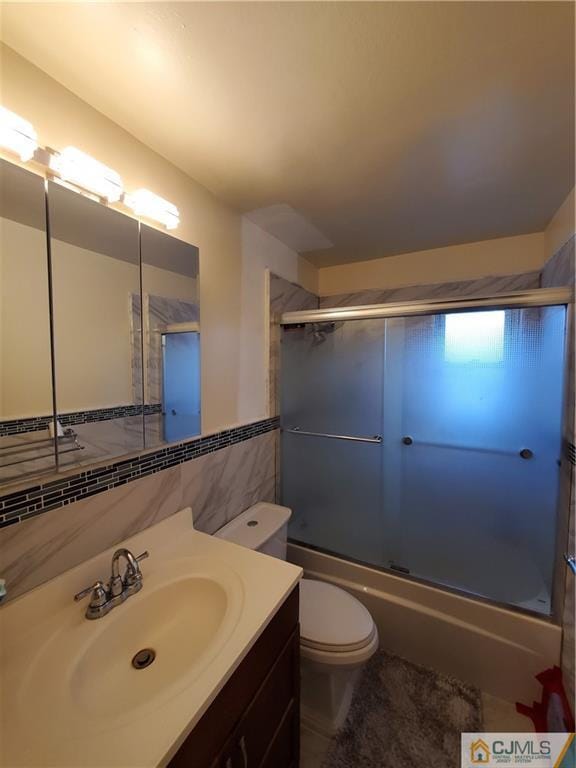 full bath with shower / bath combination with glass door, vanity, toilet, and tile walls