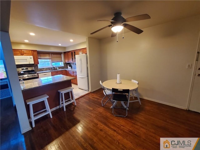 kitchen featuring white appliances, tasteful backsplash, brown cabinetry, dark wood finished floors, and a peninsula