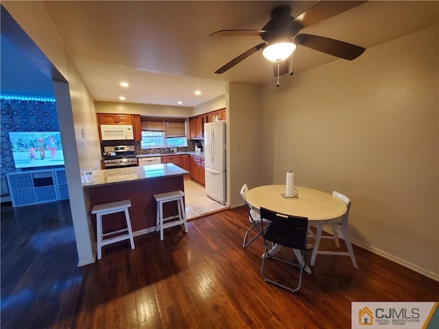 kitchen with white appliances, baseboards, brown cabinetry, wood finished floors, and a peninsula