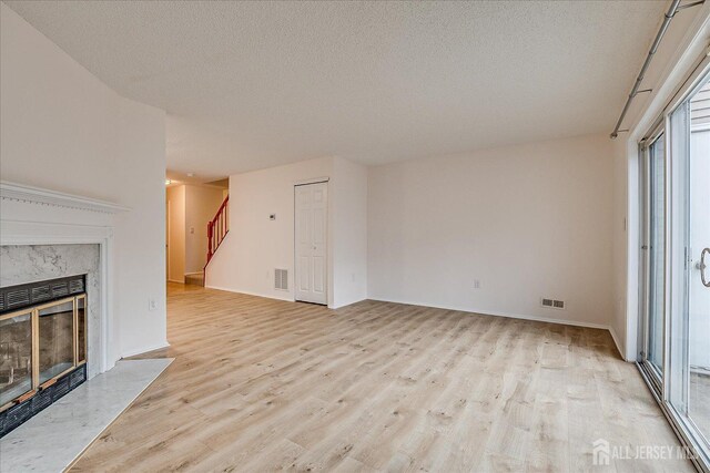 unfurnished living room featuring a textured ceiling, visible vents, a high end fireplace, stairway, and light wood finished floors