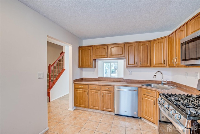 kitchen with light tile patterned floors, a textured ceiling, stainless steel appliances, a sink, and brown cabinetry