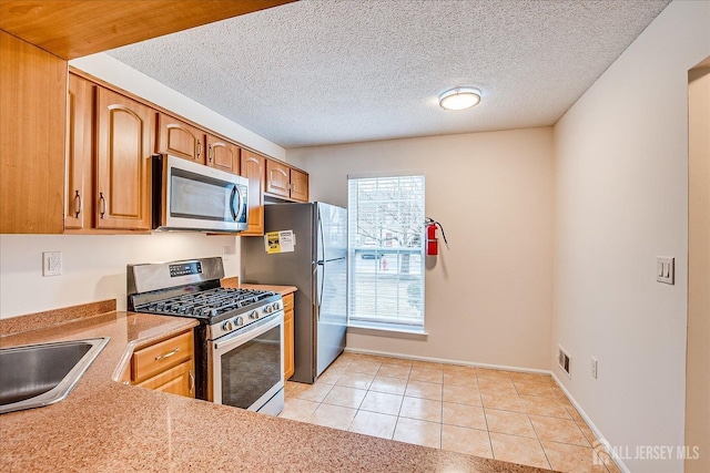 kitchen with stainless steel appliances, light countertops, light tile patterned flooring, a sink, and a textured ceiling