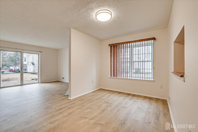 unfurnished room featuring baseboards, a textured ceiling, and light wood finished floors